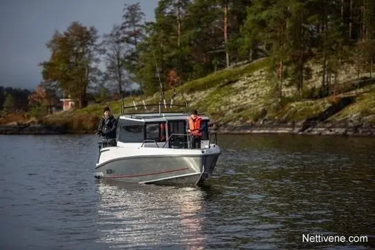 Two fishermen on a boat in calm waters, surrounded by trees and a rocky shore, enjoying a day of fishing.